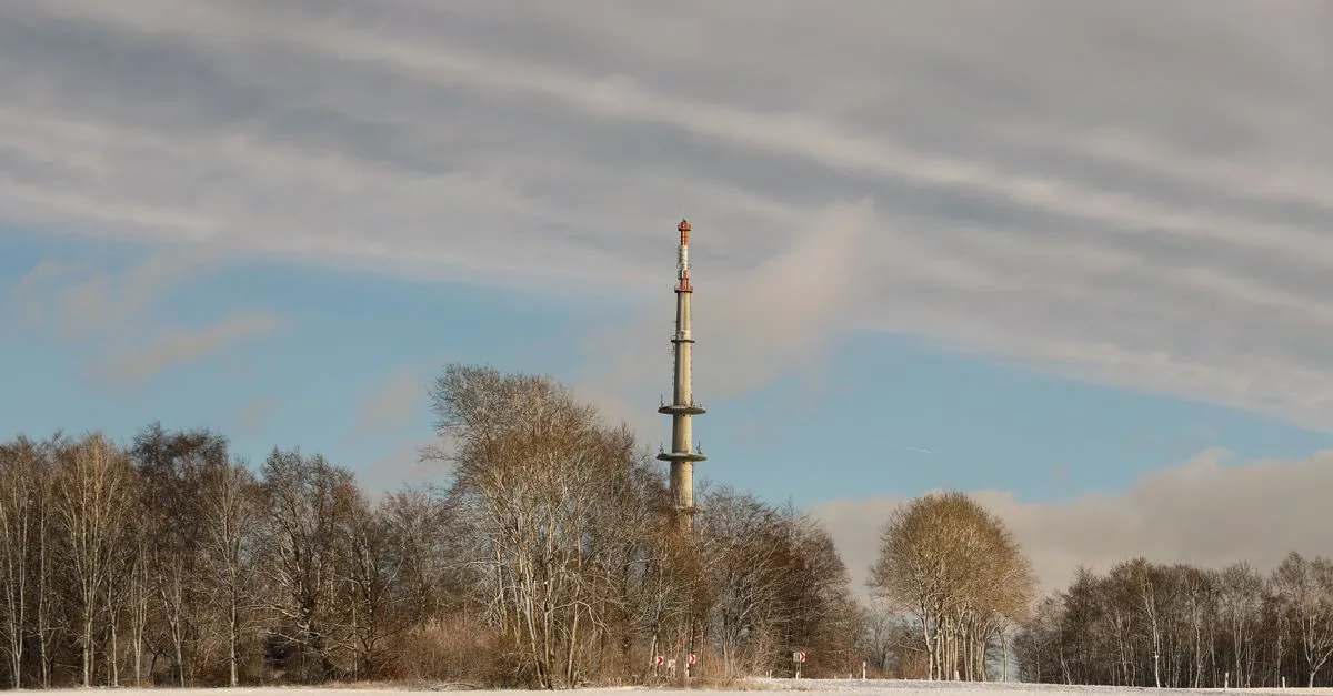 A tall communications mast rising above trees in the countryside